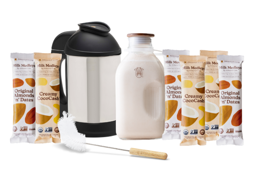 The Almond Cow Milk Maker with Glass Jug and Cleaning Brush surrounded by Almond 'n' Dates and Creamy CocoCash Milk Medleys