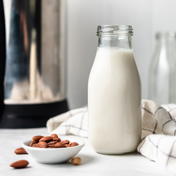 homemade almond milk in a glass bottle, next to a bowl of almonds and the almond cow milk maker