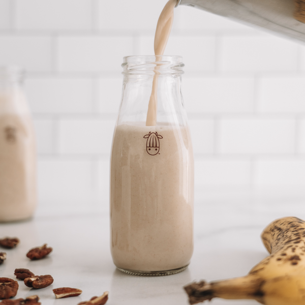 glass of plant-based banana bread milk being poured in a glass bottle
