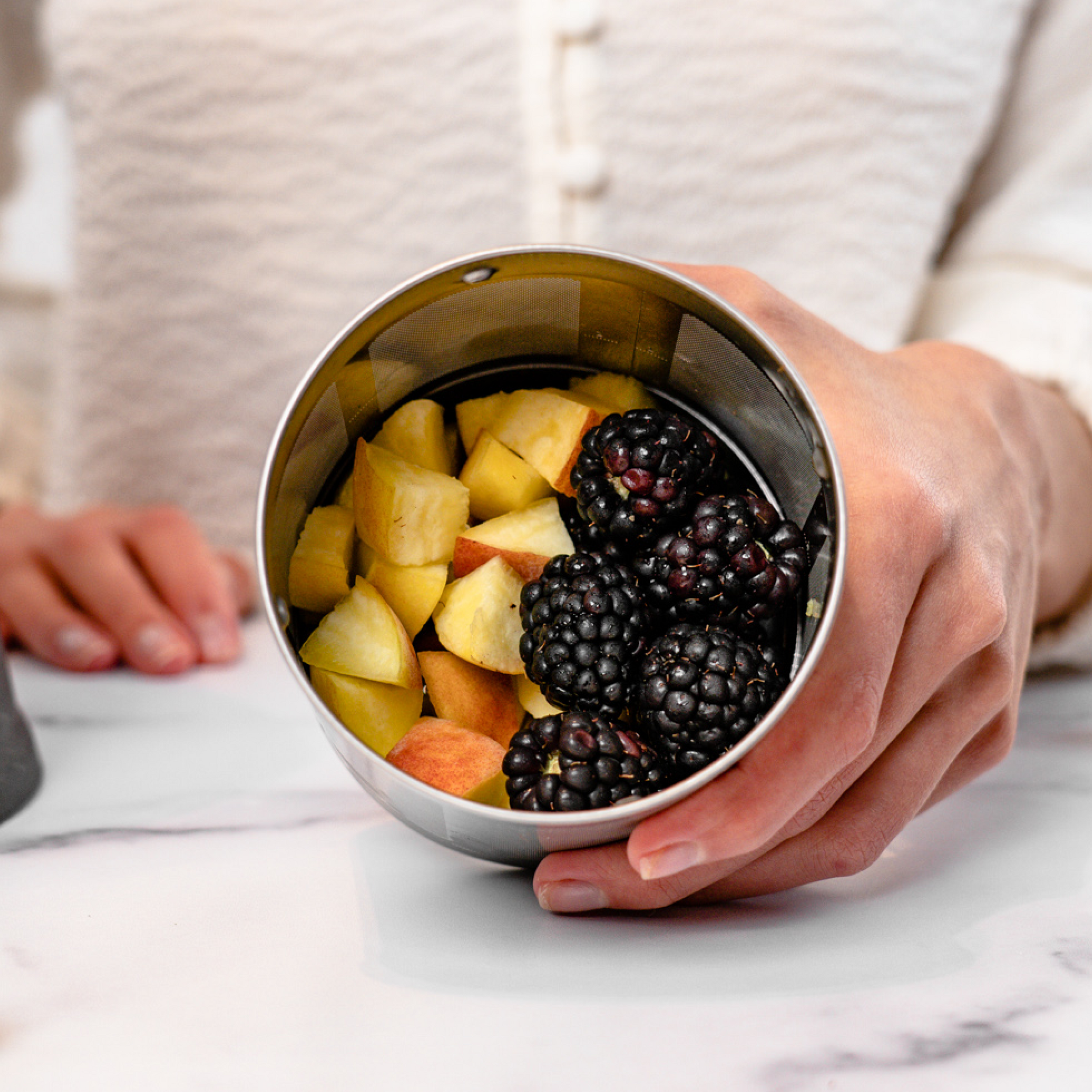 person holding filter basket full of peaches and blackberries