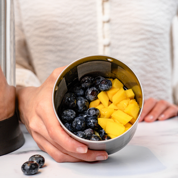 person holding filter basket full of blueberries and mango pieces