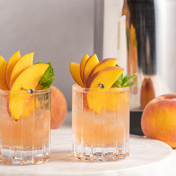 Bourbon Peach Smash in a glass garnished with peach slices and mint