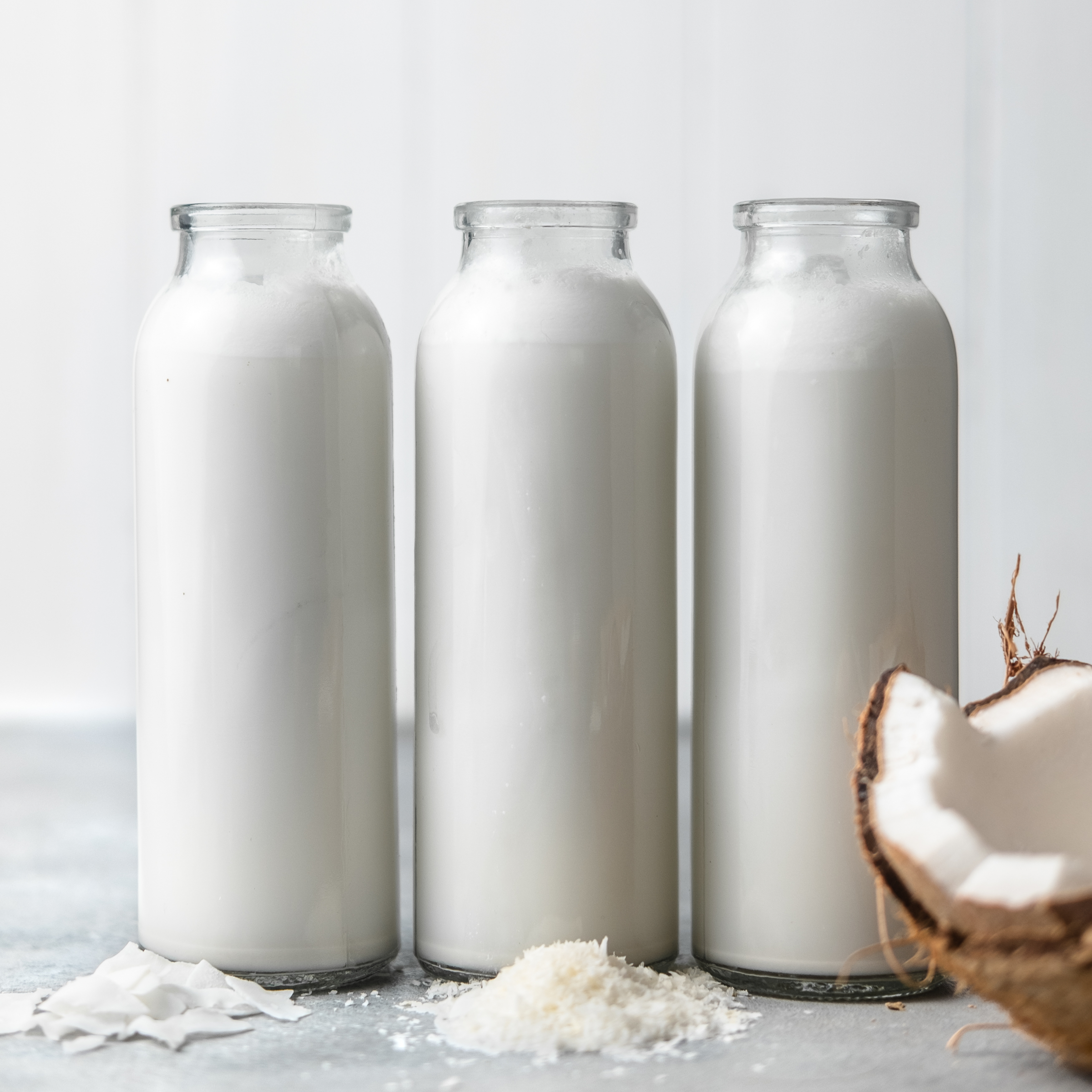 homemade coconut milk in three jugs next to a coconut