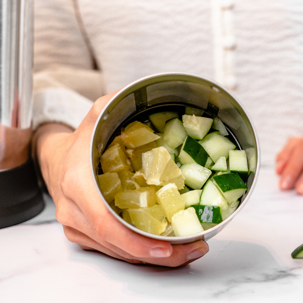 person holding filter basket full of cucumber and lemon pieces