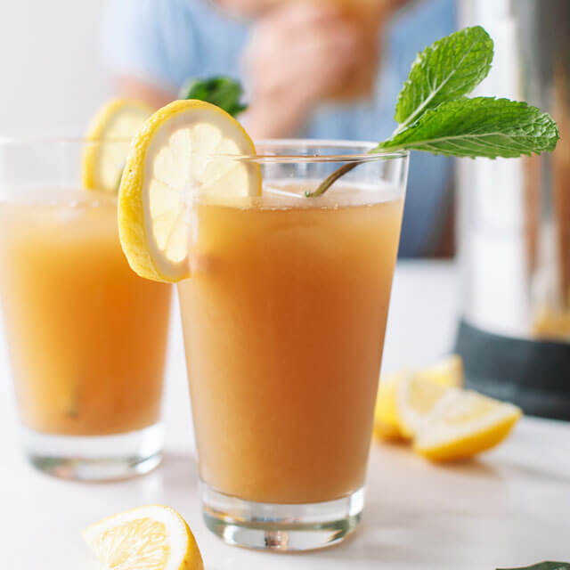 a glass of Tea Lemonade with a lemon and sprig of mint