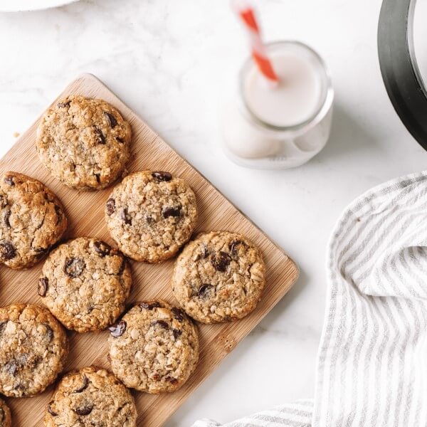 a board of vegan Oatmeal Chocolate Chip Cookies with a glass of plant-based milk