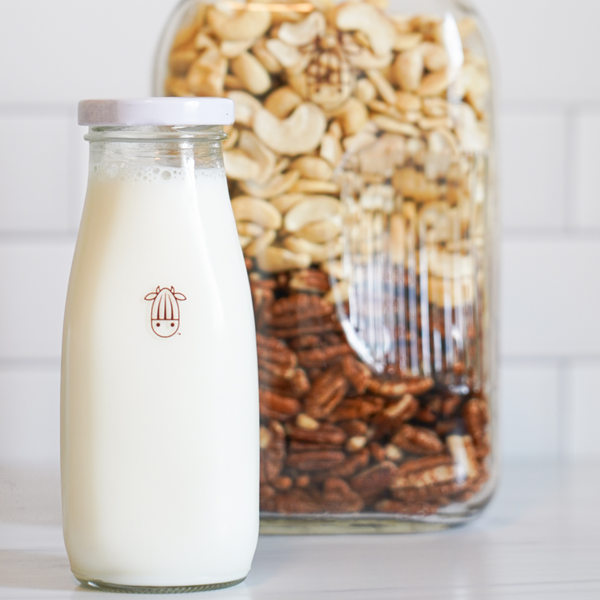 glass jug filled with cashews and pecans and a small bottle of PeCashew plant-based milk