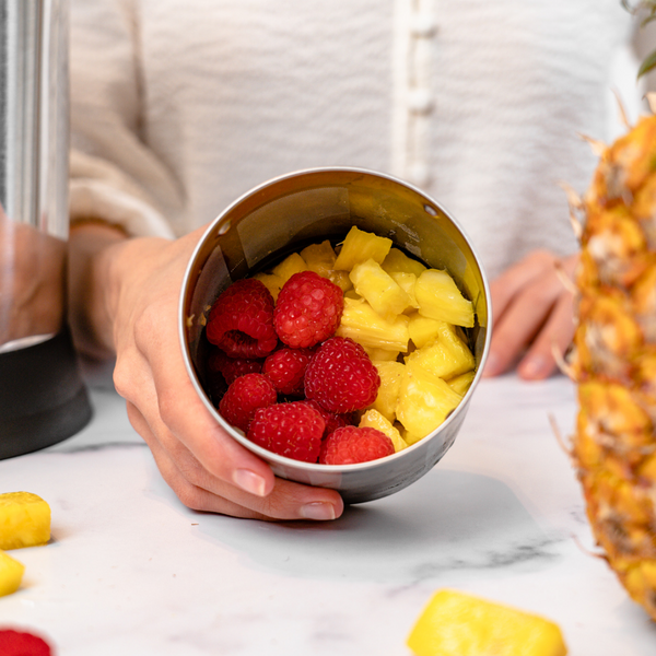 person holding filter basket full of raspberries and pineapple