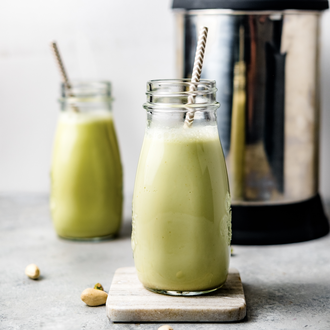 homemade pistachio milk in two glasses with straws, next to the almond cow milk maker