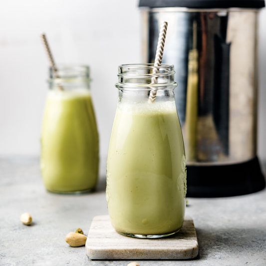 homemade pistachio milk in two glasses with straws, next to the almond cow milk maker