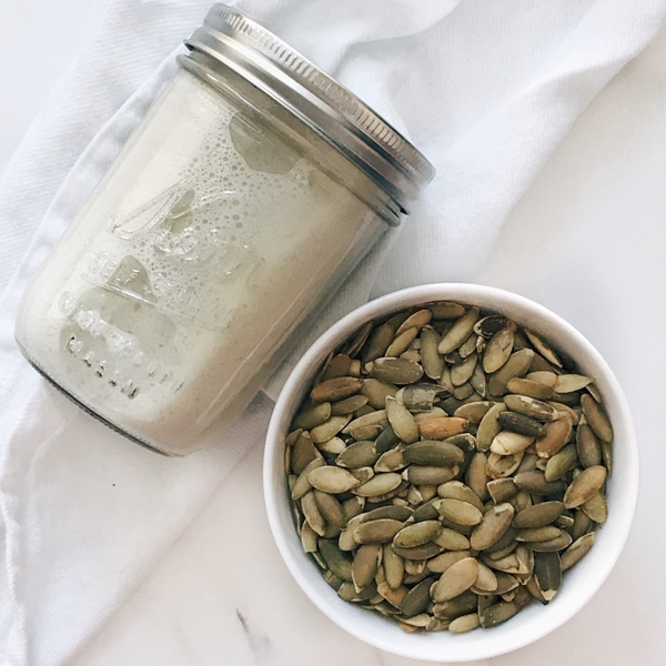 homemade pumpkin seed milk in a jar with a small bowl of pumpkin seeds on the side