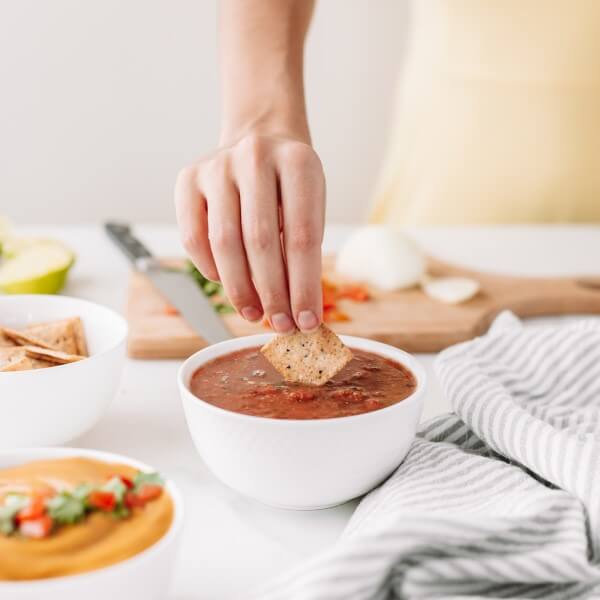 a chip being dipped into a bowl of pumpkin seed pulp salsa