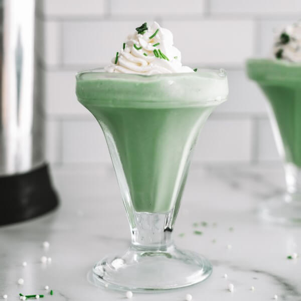 plant-based shamrock shake in a glass garnished with coconut whipped cream and sprinkles