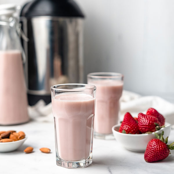 a jug and two glasses with homemade strawberry almond milk, next to almonds and strawberries