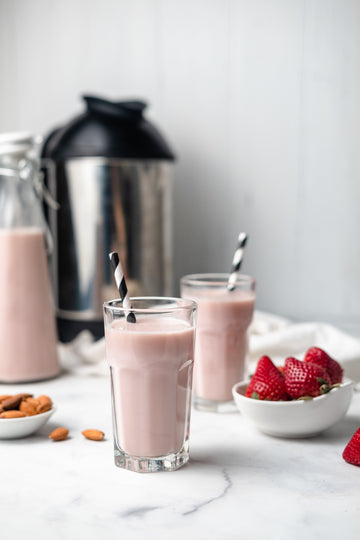 a jug and two glasses with homemade strawberry almond milk, next to almonds and strawberries