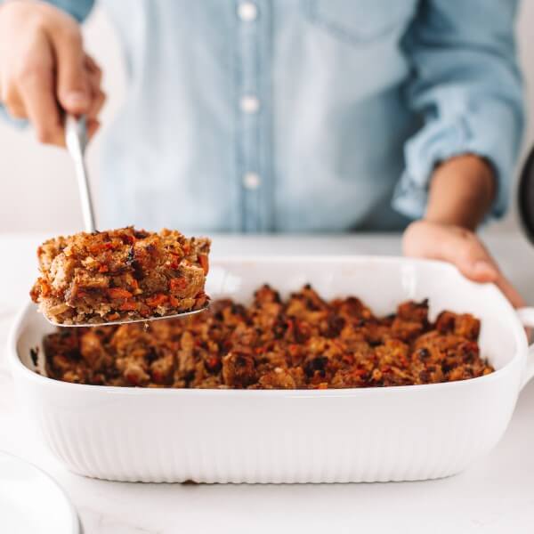 a person serving a baking tray of vegan stuffing